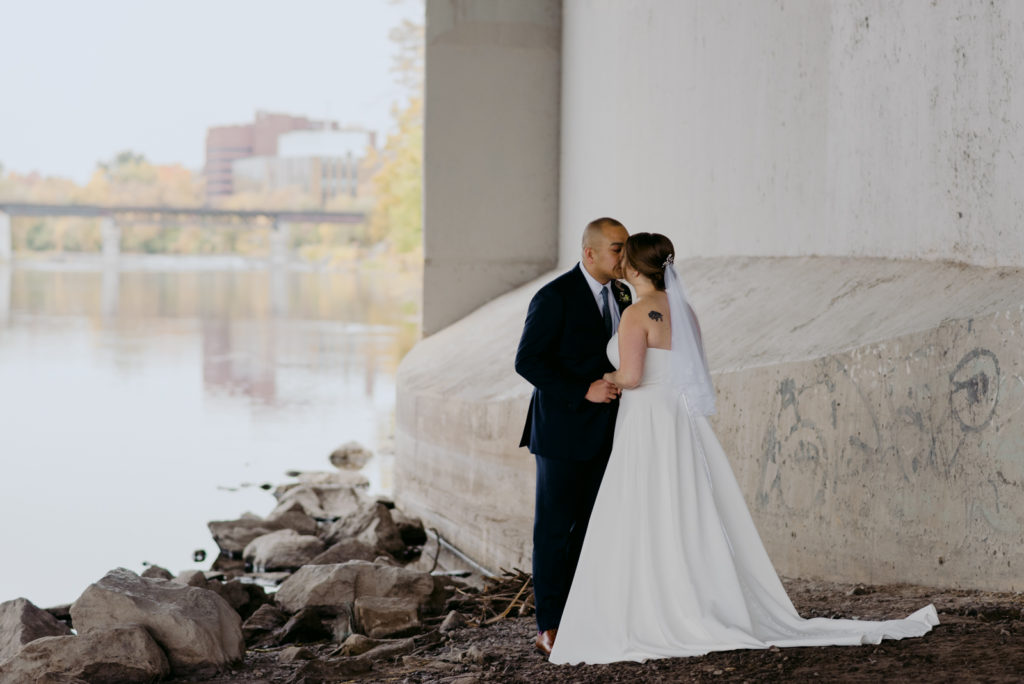bride and groom kissing underneath a bridge on a rainy day