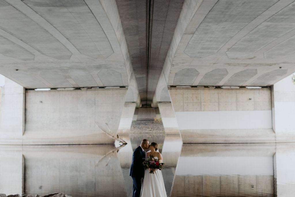 bride and groom kissing underneath a bridge