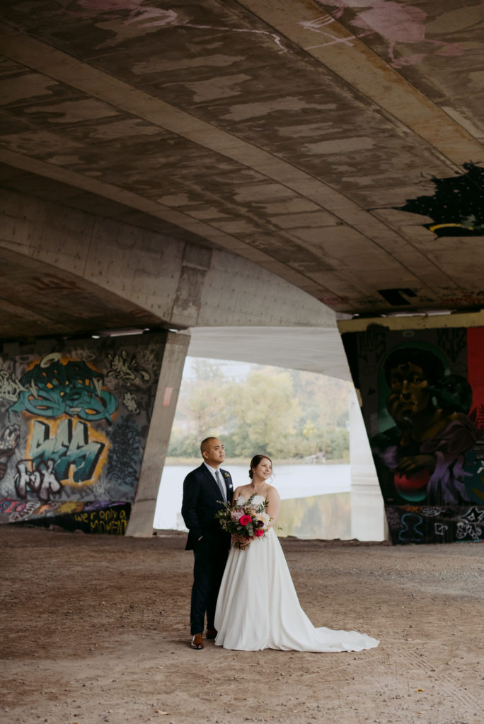 bride and groom underneath a bridge with graffiti