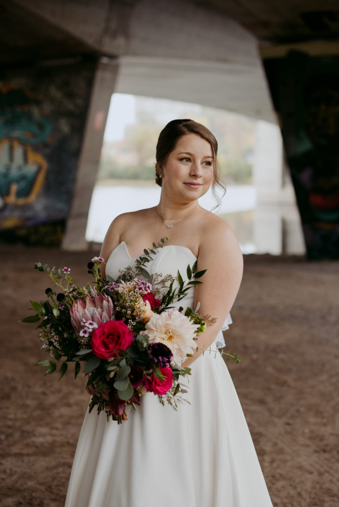 bride holding a wild bouquet underneath a bridge with graffiti