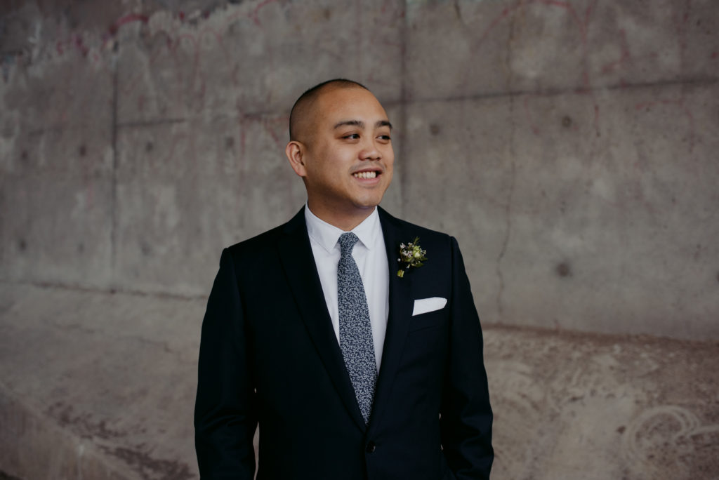 groom smiling standing against a concrete wall