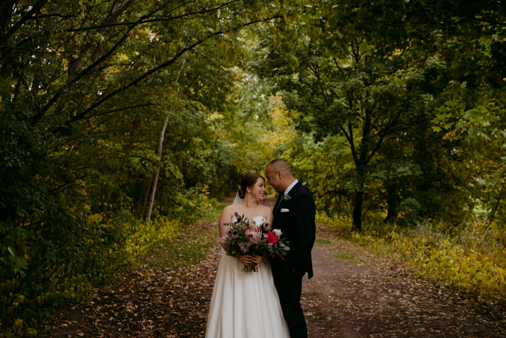 bride and groom standing underneath trees on a rainy day smiling