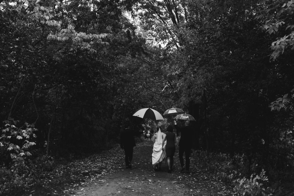 bride and groom with their wedding party holding umbrellas over their heads walking down a path