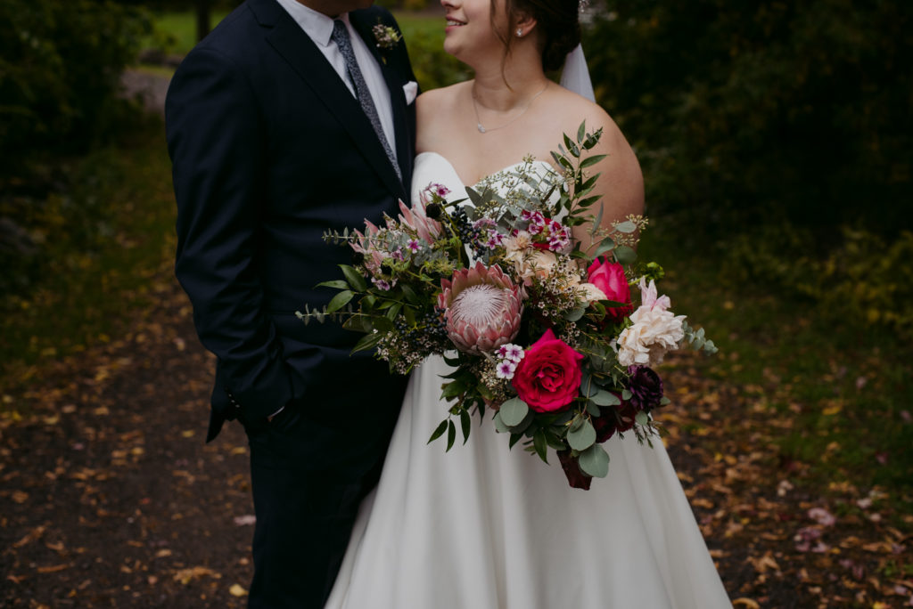 bride and groom on a path in the woods holding wild bouquet