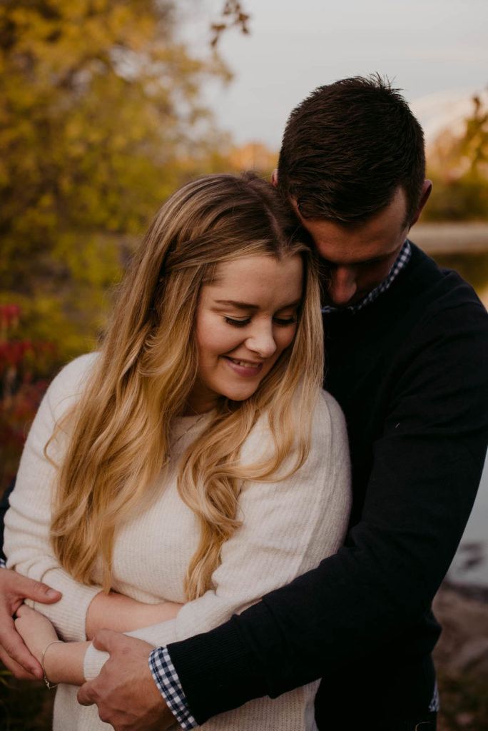 engaged couple with arms around each other outdoors in the fall