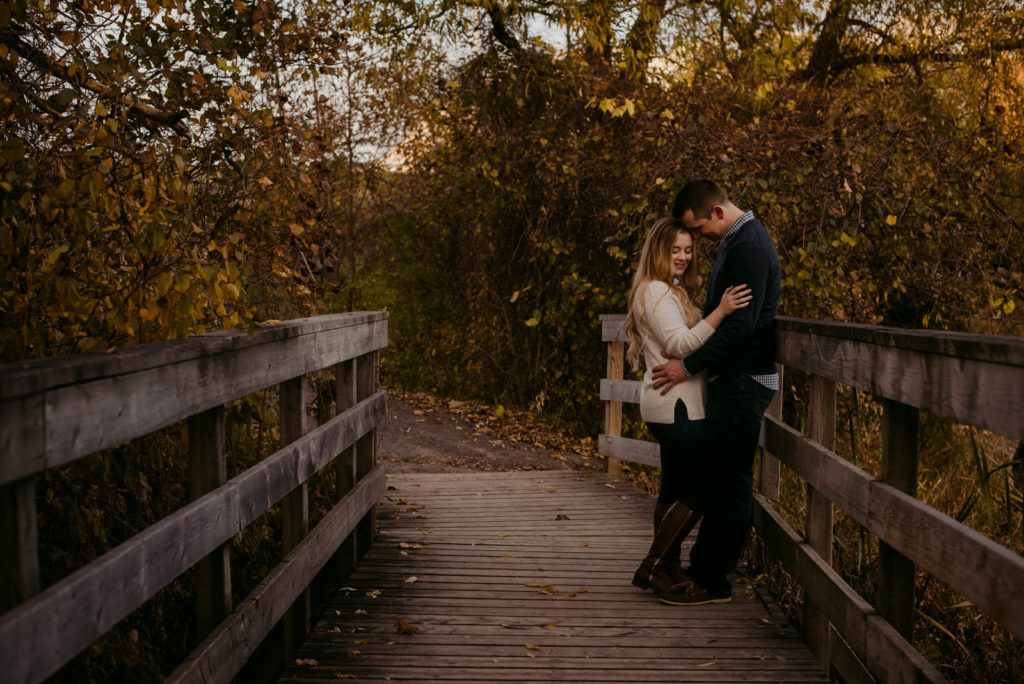 engaged couple cuddling close on a wooden bridge in the fall