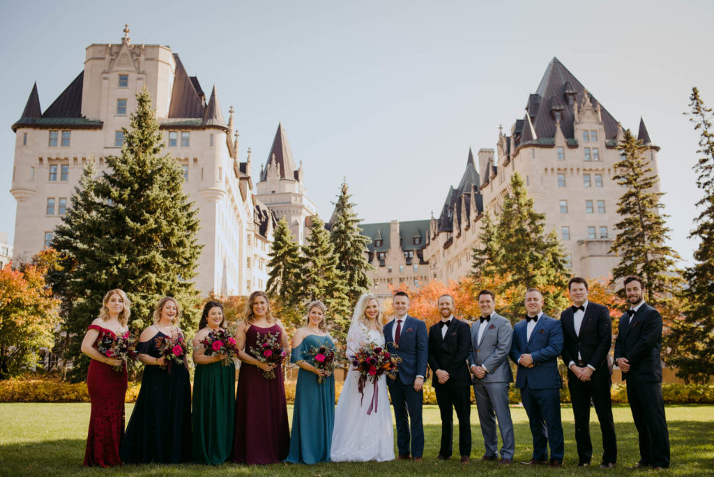 wedding party wearing colourful dresses outside of the chateau laurier in majors hill park