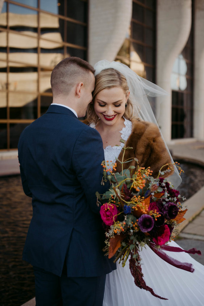 bride wearing fur shawl holding a wild bouquet cuddling with her husband