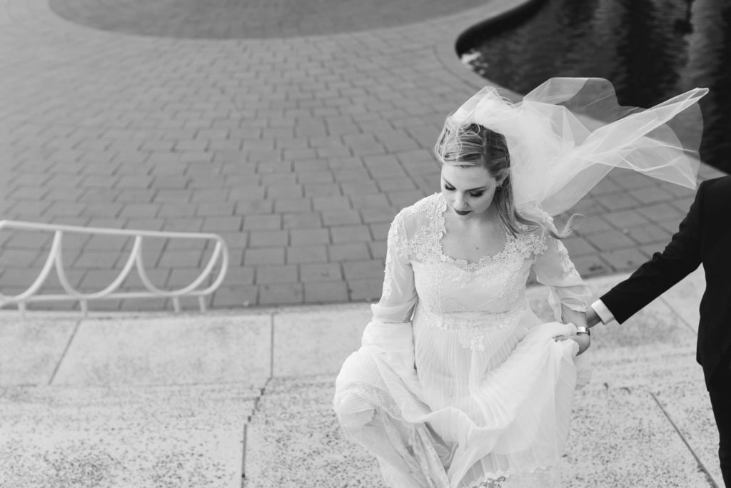 bride's veil blowing in the wind as she walks up the stairs