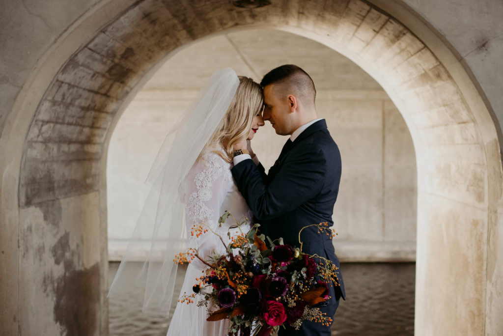 bride and groom cuddling underneath concrete arch