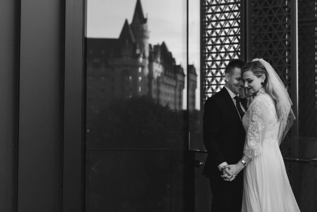 bride and groom cuddling with the Chateau Laurier reflected in the background at the NAC in Ottawa