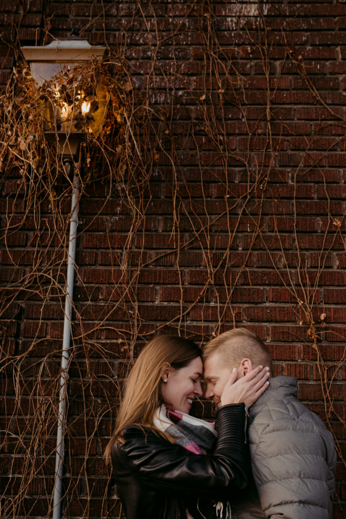 engaged couple cuddling close by old light fixture wrapped in vines