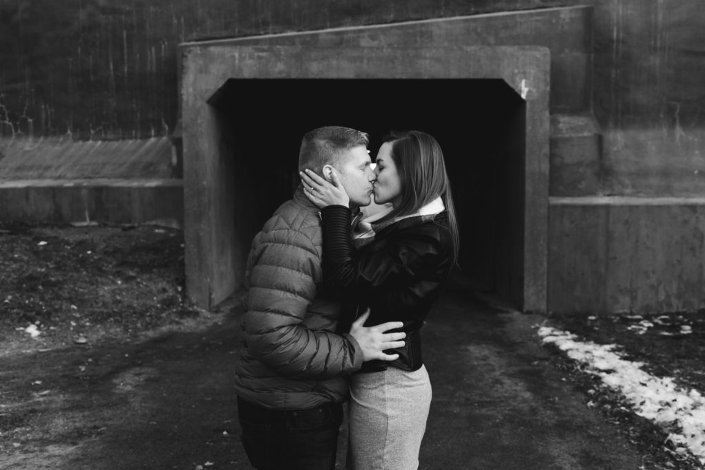 engaged couple kissing by a bridge in black and white