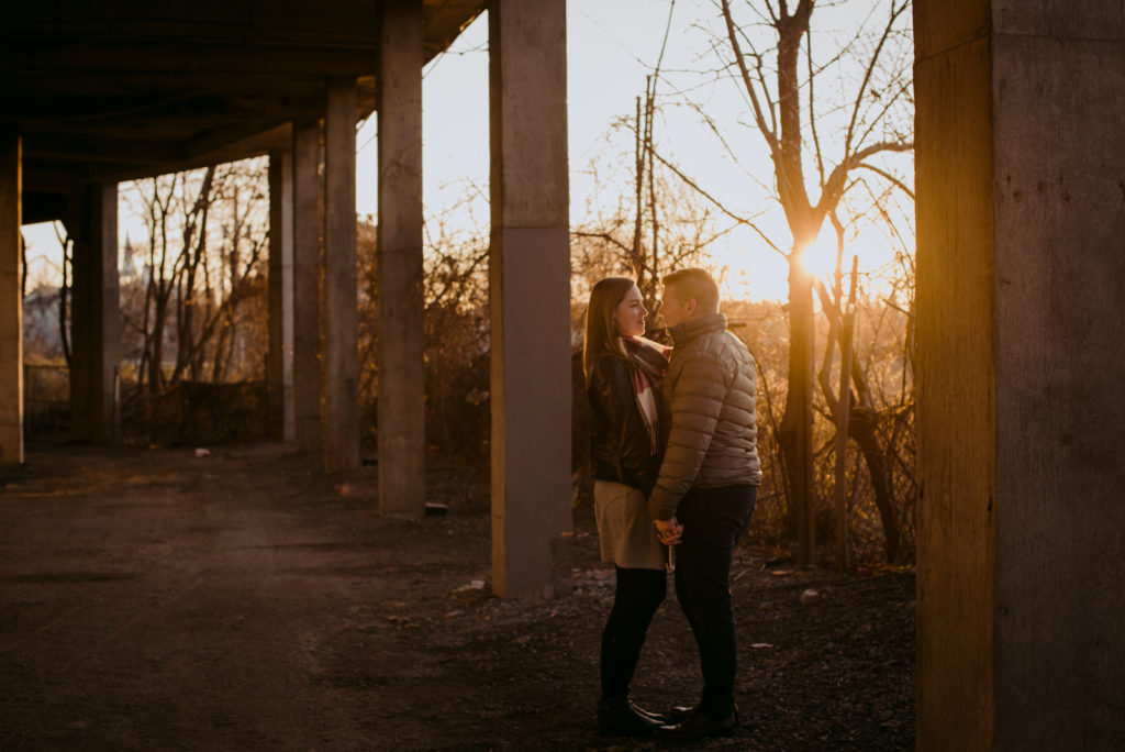 engaged couple underneath a bridge at sunset