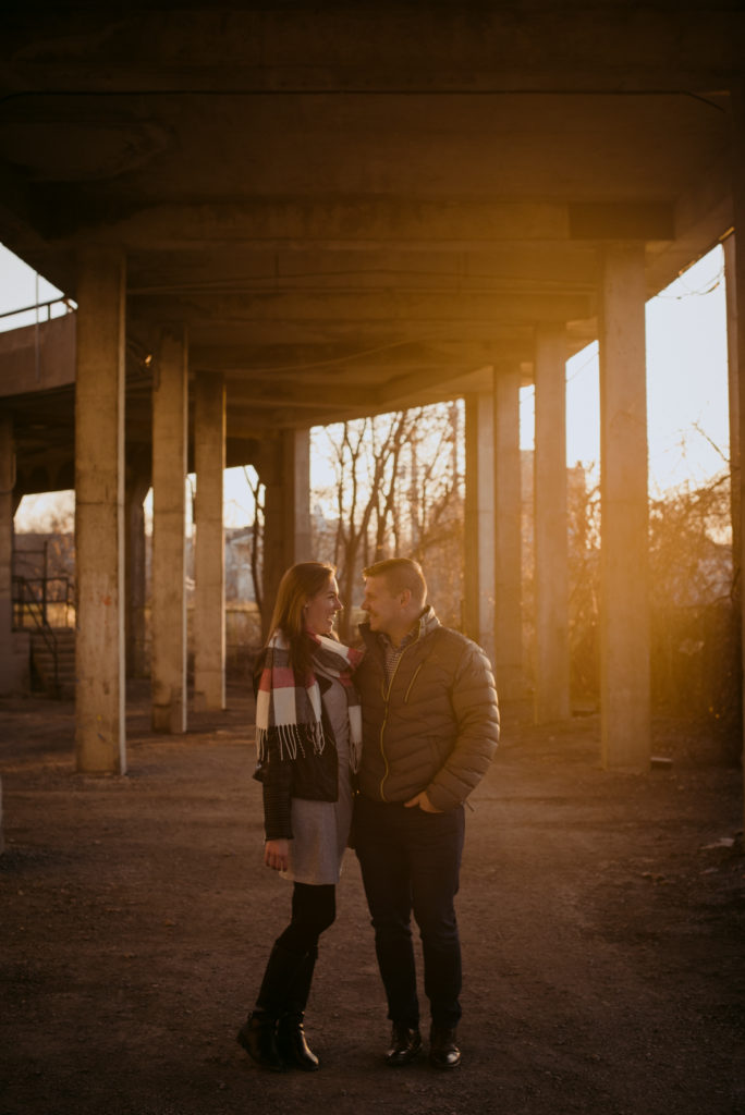 engaged couple underneath a bridge at sunset