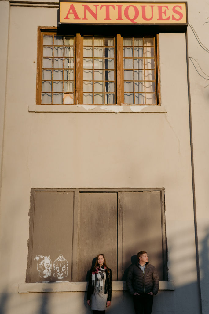 engaged couple standing below antique store sign in the shadows