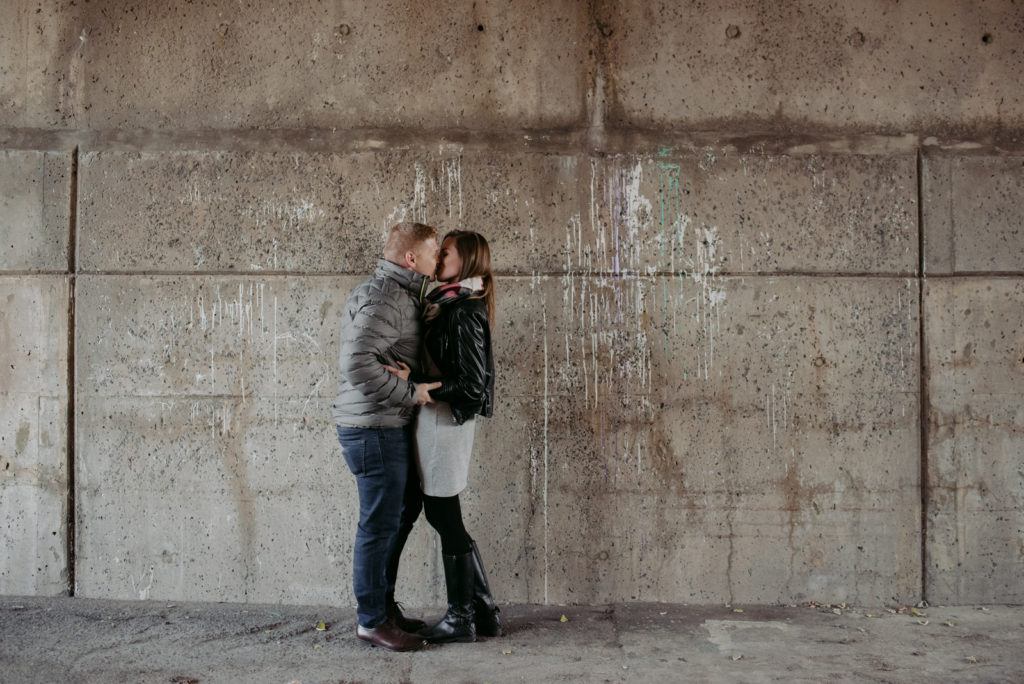 engaged couple kissing against concrete wall with paint