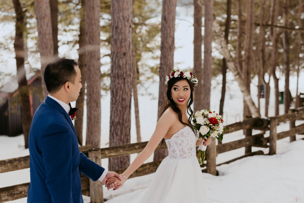 bride and groom walking together down wooded path in the winter