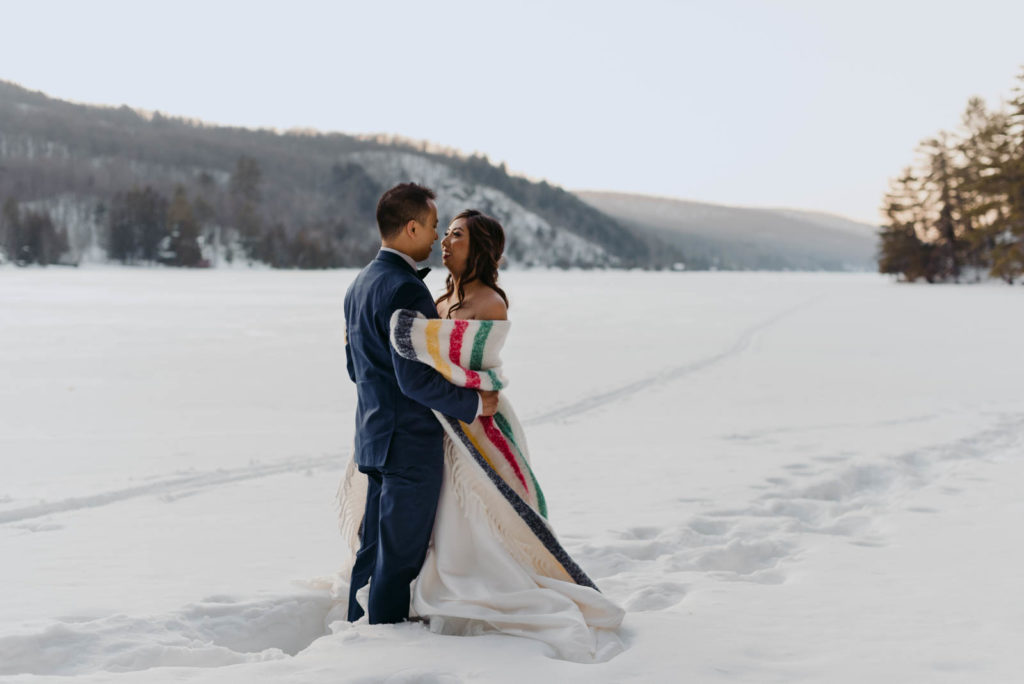 bride and groom on frozen lake at sunset with hudson's bay blanket