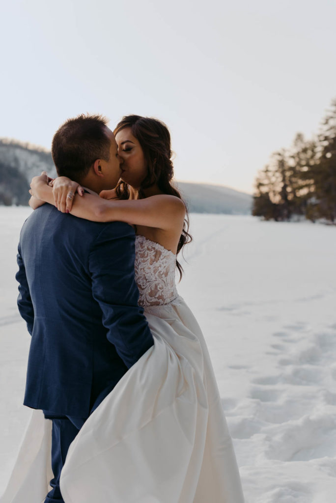 bride and groom kissing on a frozen lake at sunset