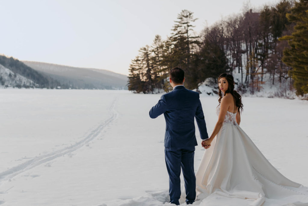 bride and groom holding hands on a frozen lake at sunset