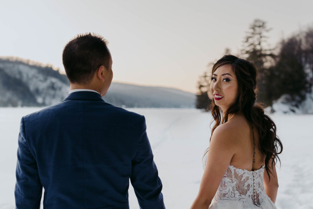 bride and groom standing on a frozen lake at sunset
