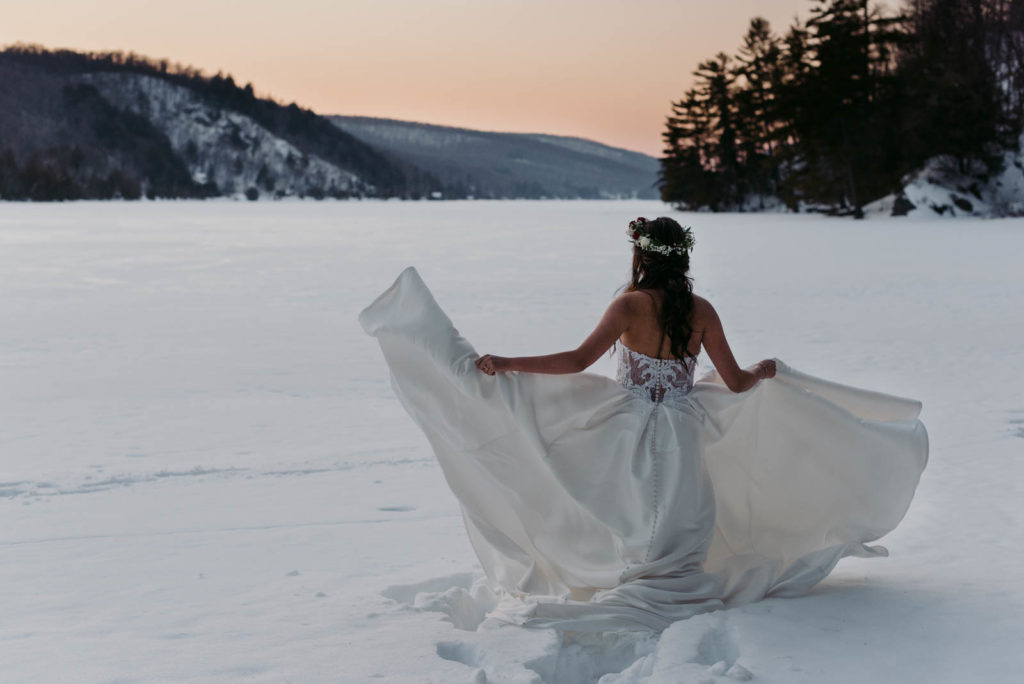 bride twirling her dress around on frozen lake at sunset