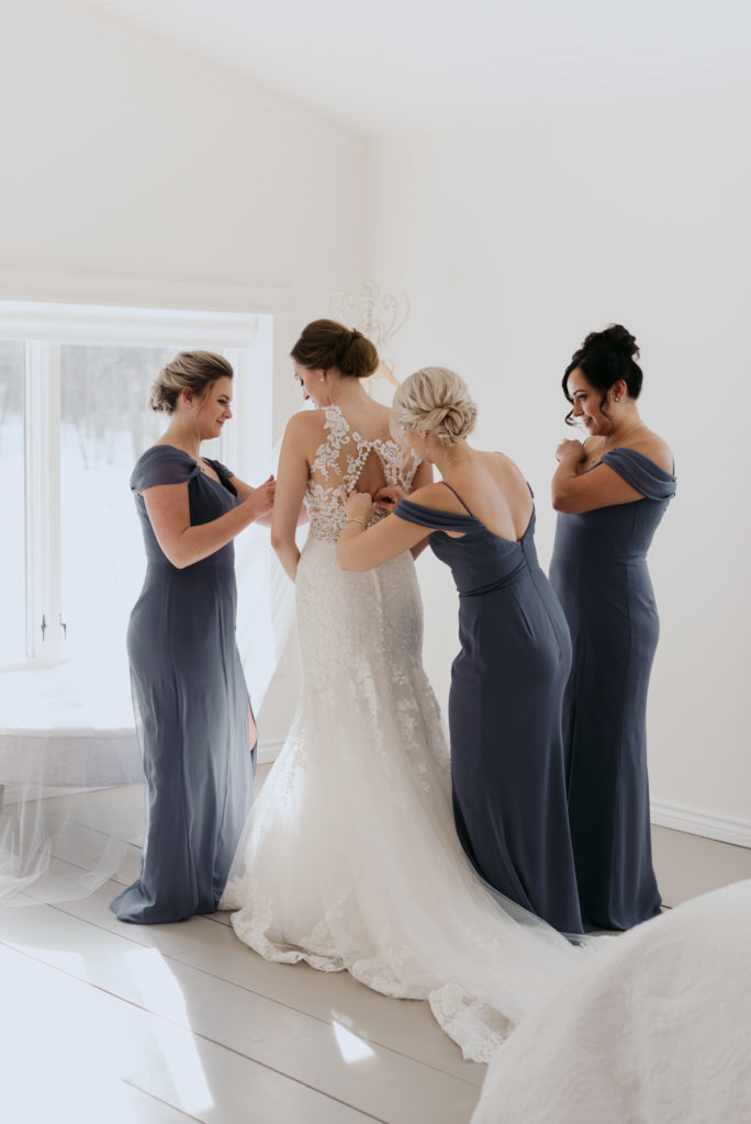bridesmaids in blue helping bride into her dress