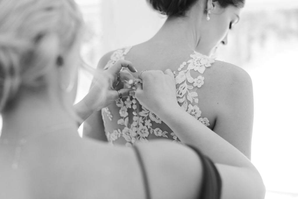 bridesmaid tying up bride's dress