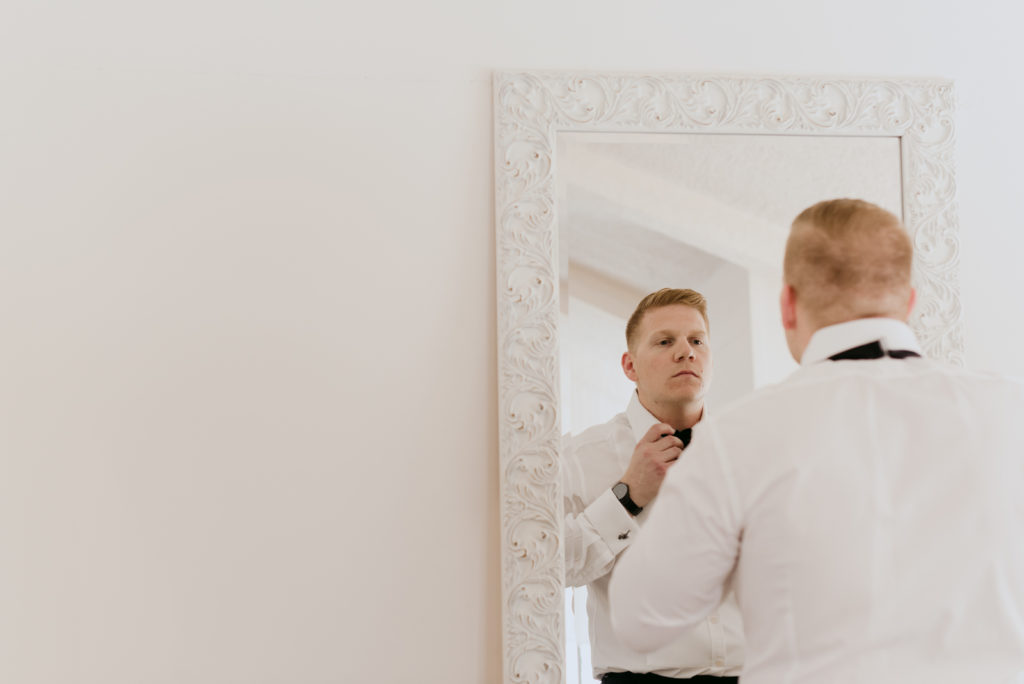 groom adjusting his bowtie in the mirror