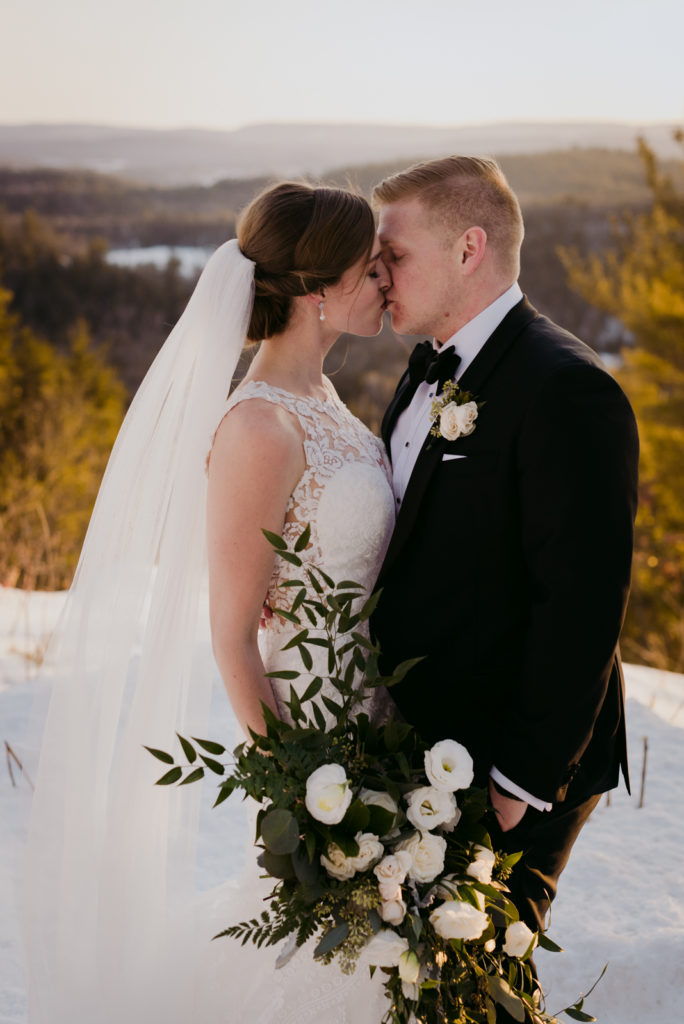 bride and groom kissing on top of a mountain overlooking the gatineau hills at le Belvedere winter wedding