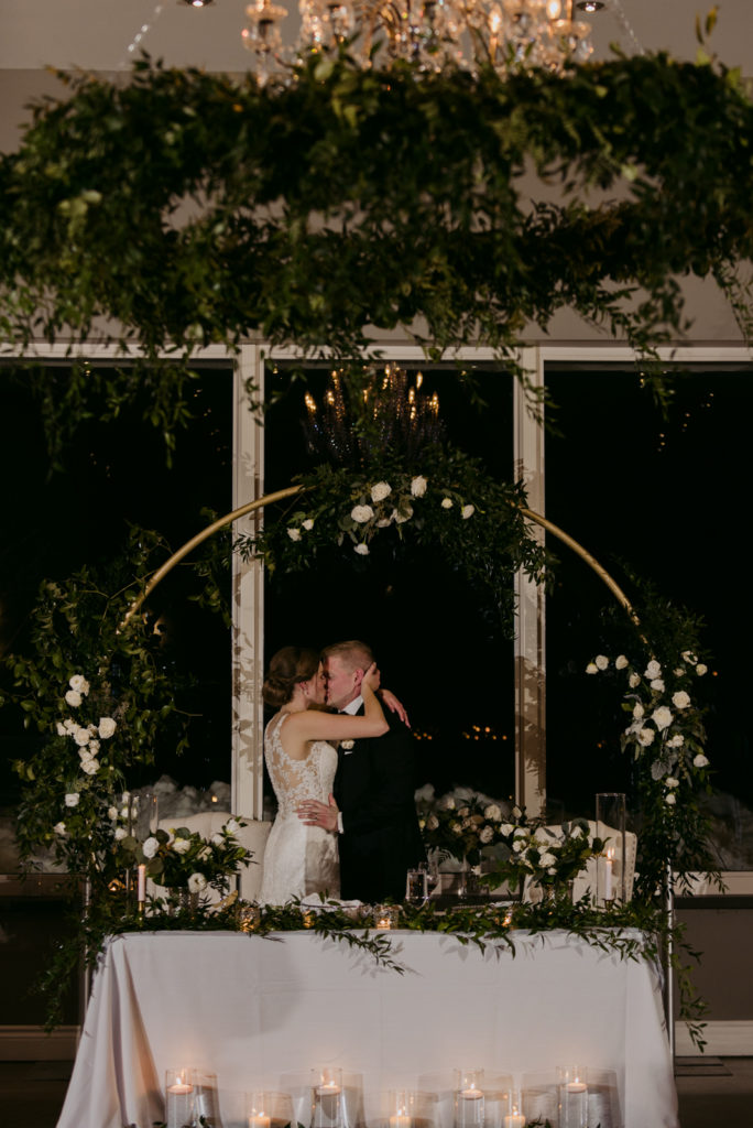 bride and groom kissing under floral arch at sweetheart table at le belvedere wedding