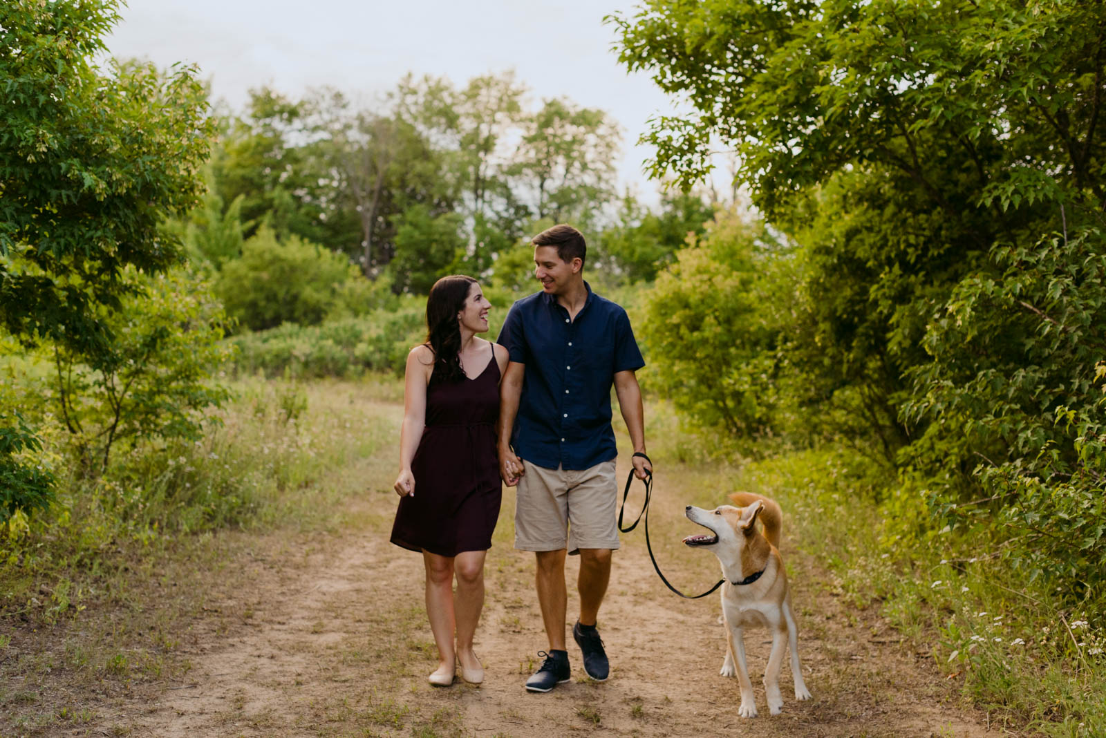 engaged couple walking their dog down a dirt trail