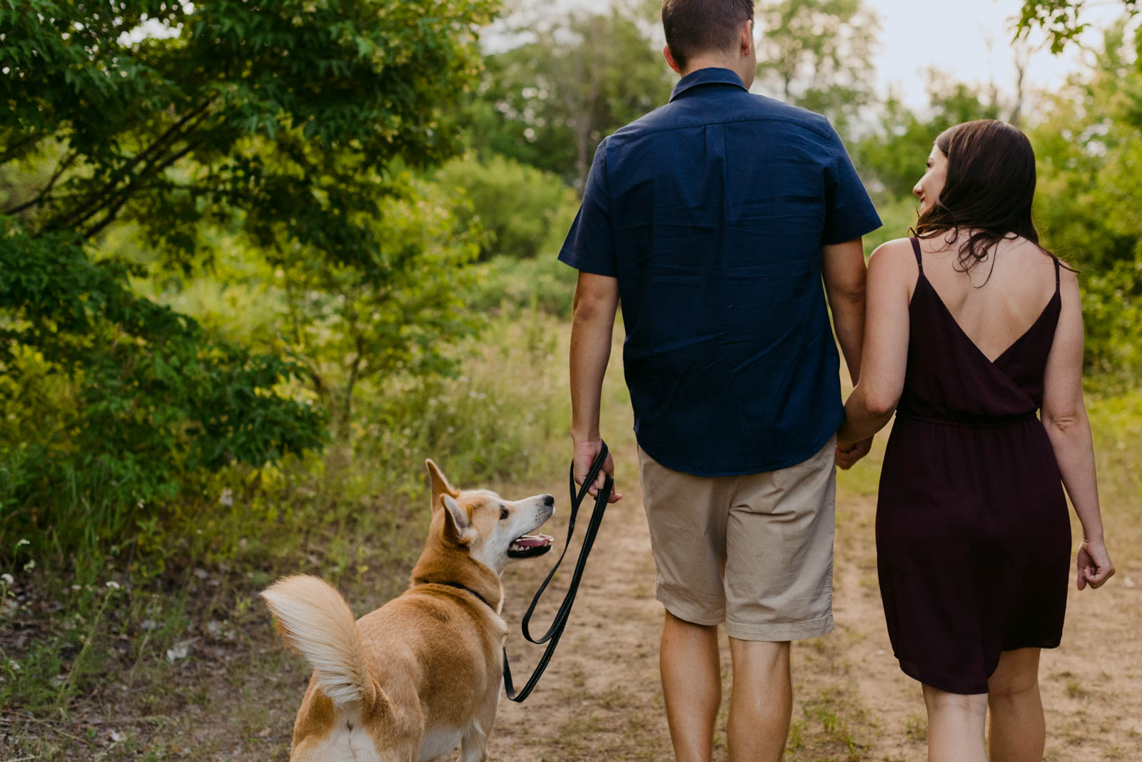 engaged couple holding hands walking their dog through a nature trail