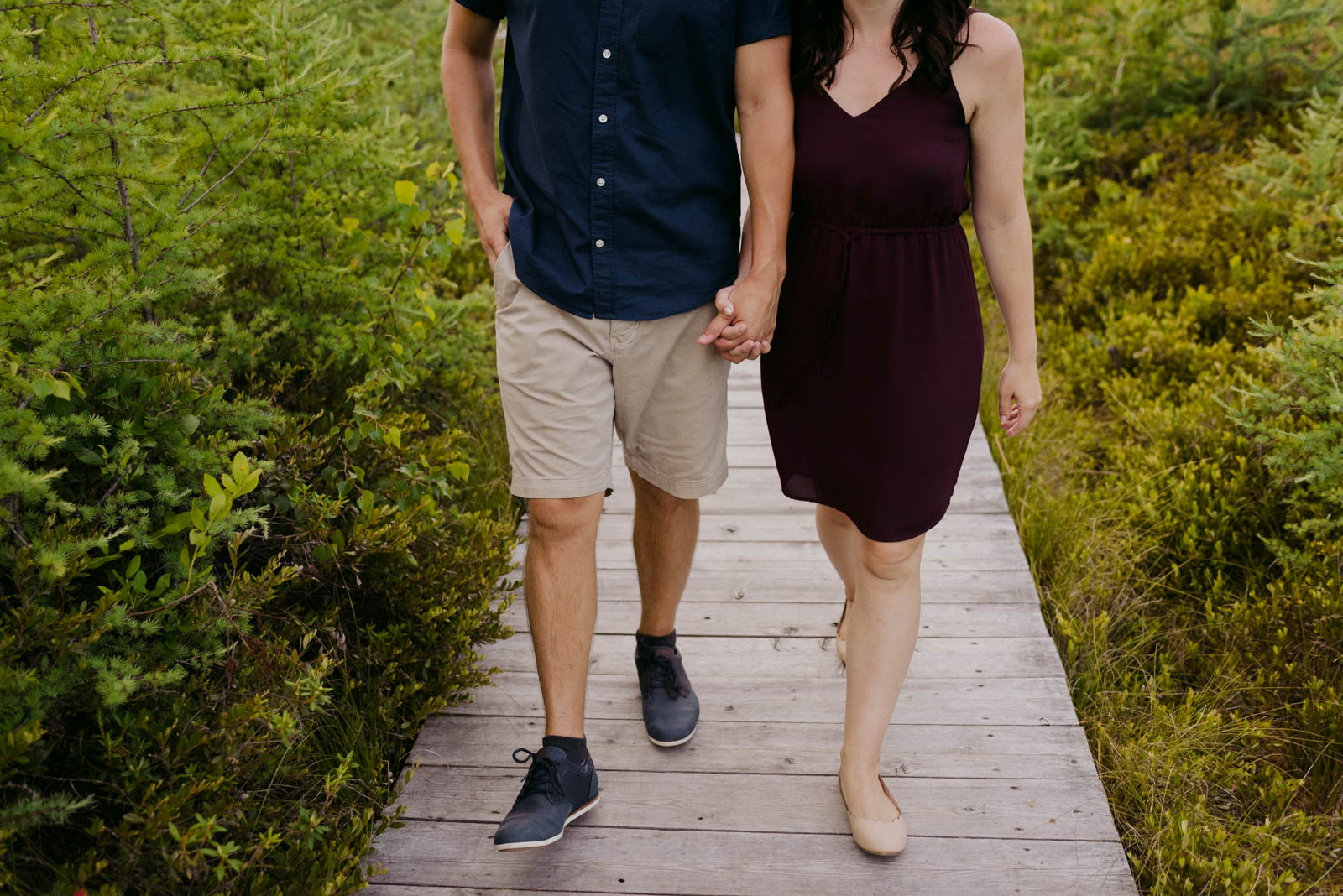 engaged couple holding hands walking down a boardwalk