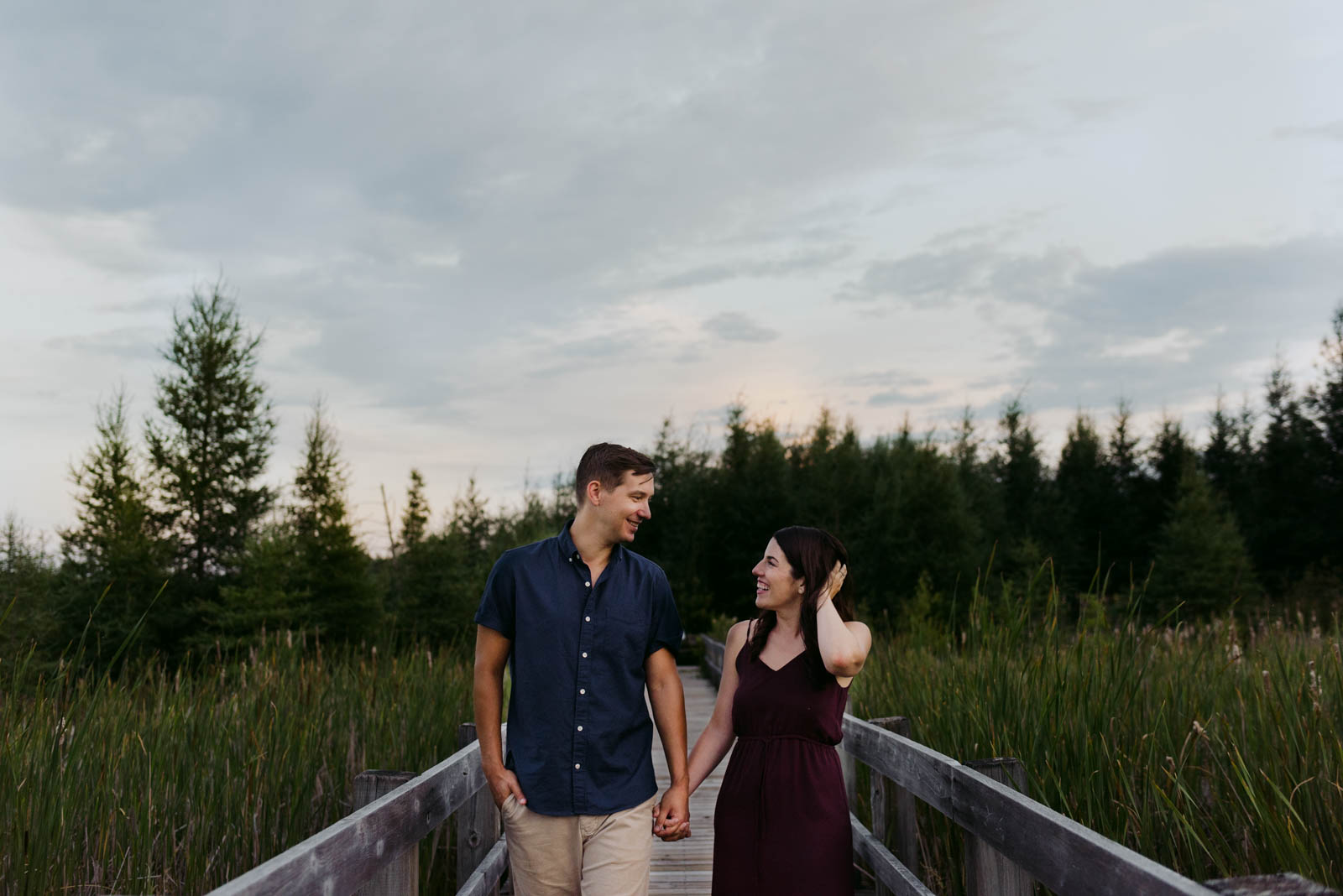 engaged couple waking down a boardwalk holding hands