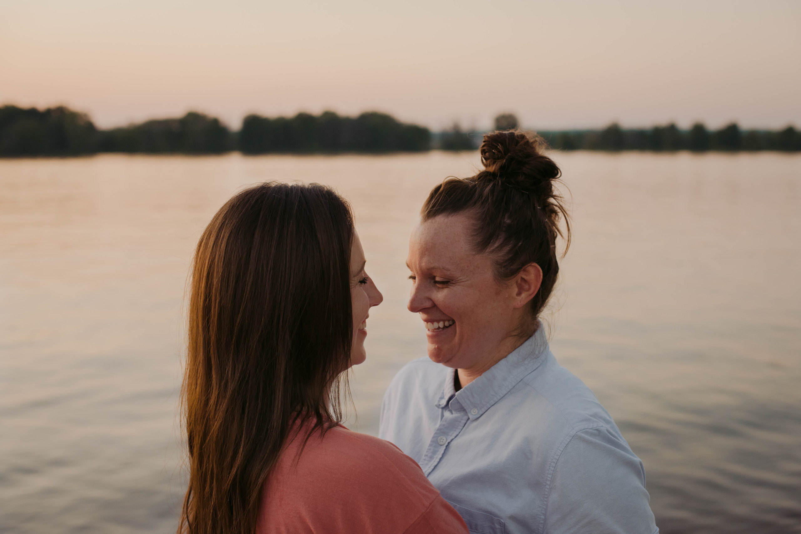 same sex couple hugging and laughing by the water at sunset