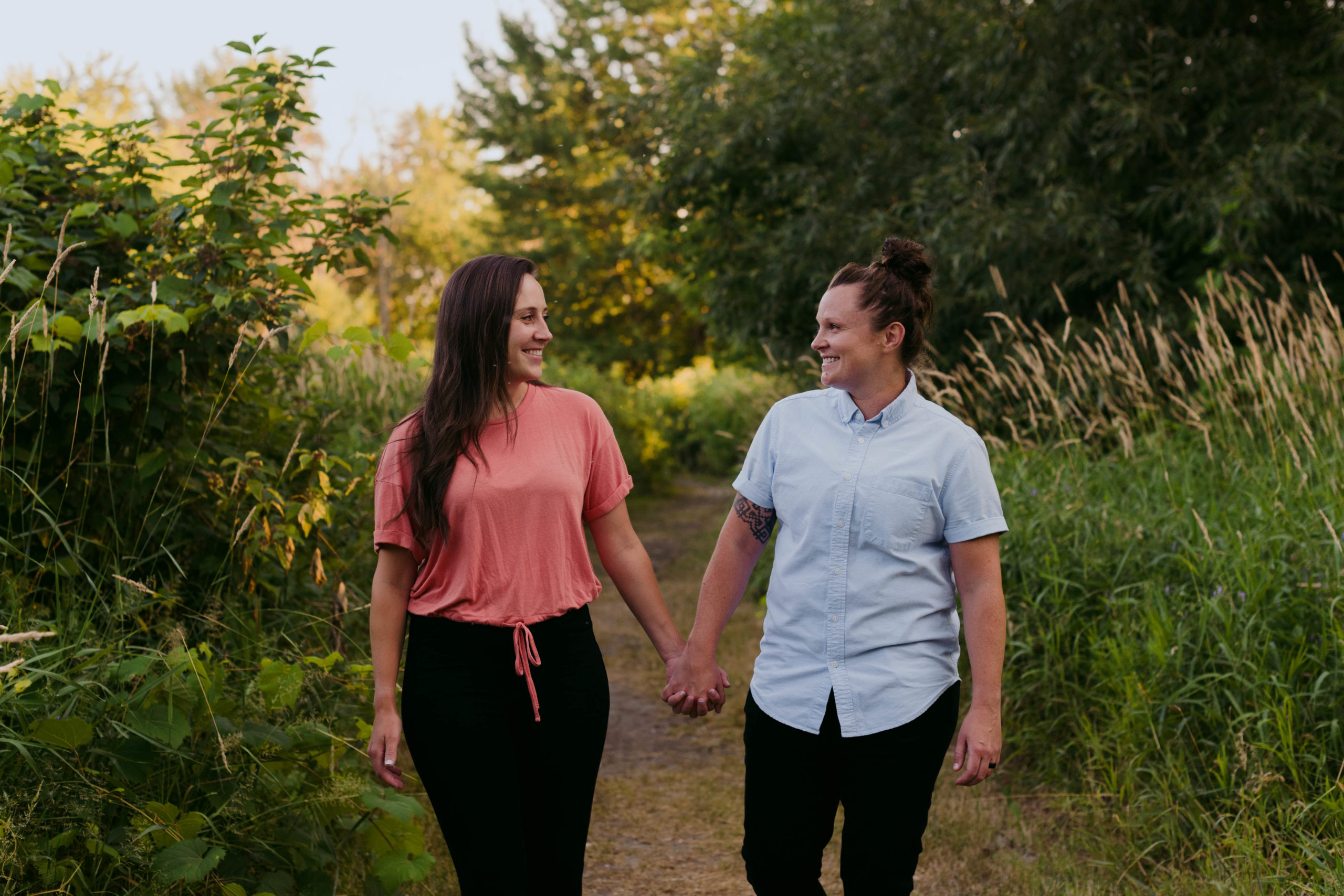 same sex couple holding hands walking down a tree lined path
