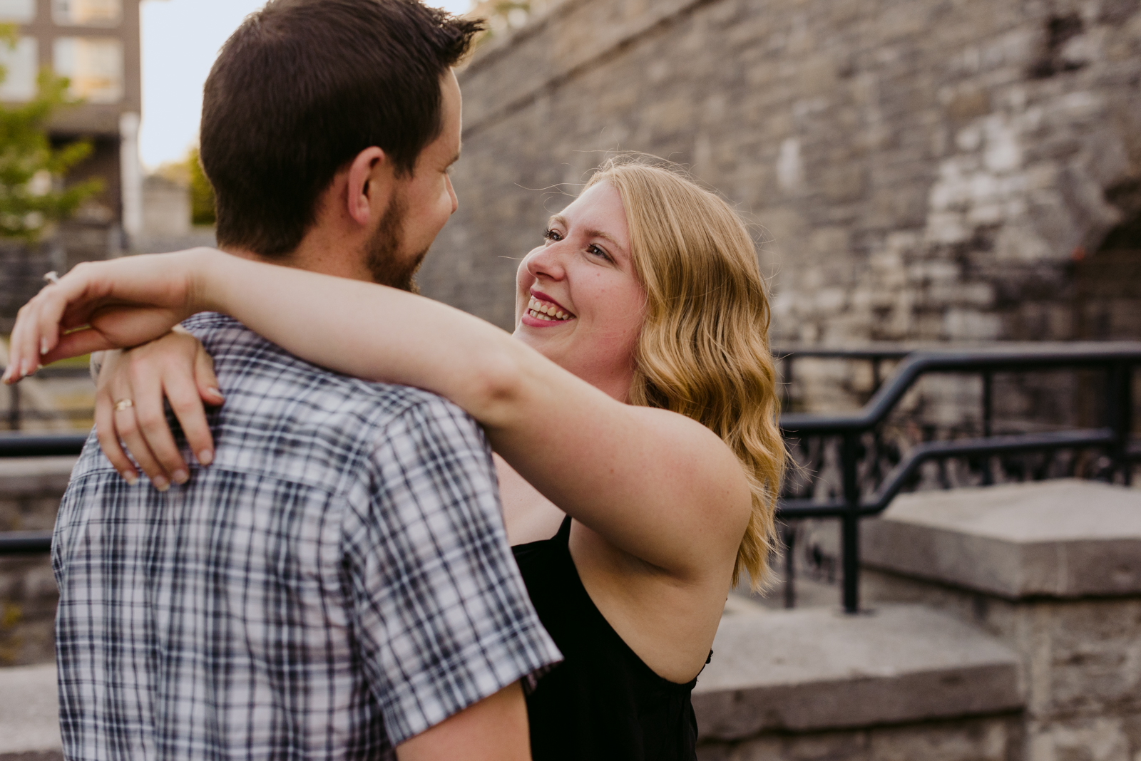 engaged couple hugging by an old brick wall at sunset