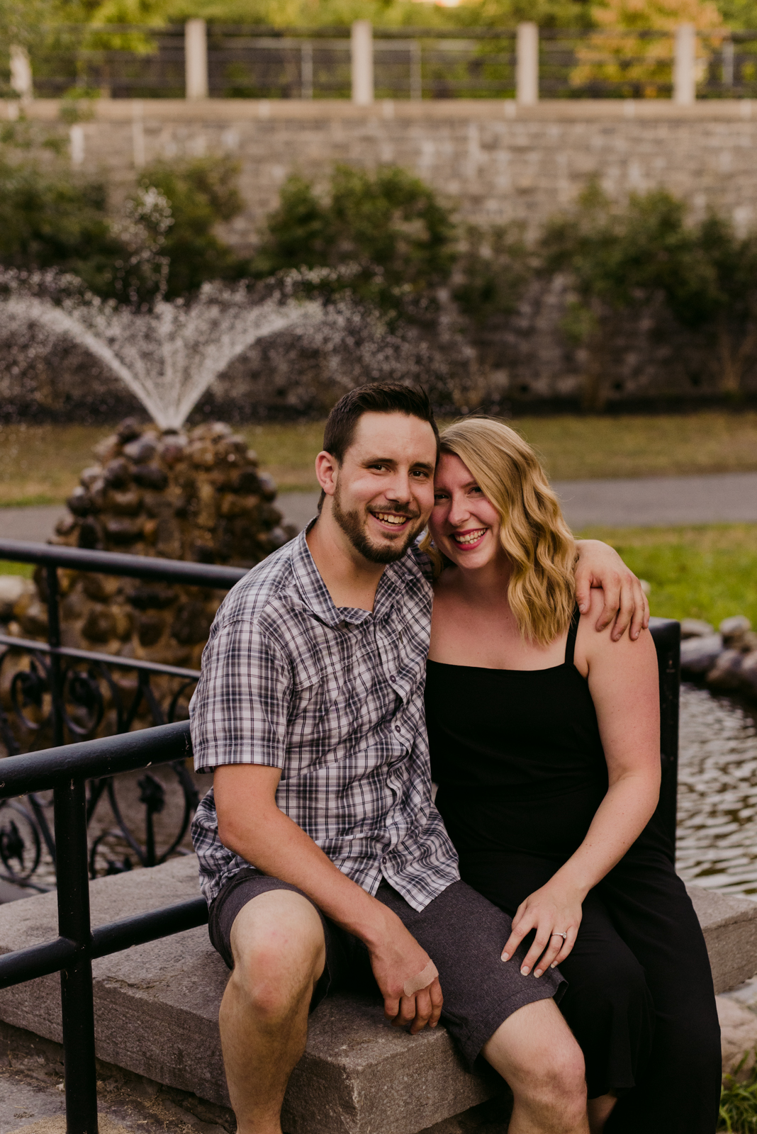 engaged couple sitting by a water fountain at sunset