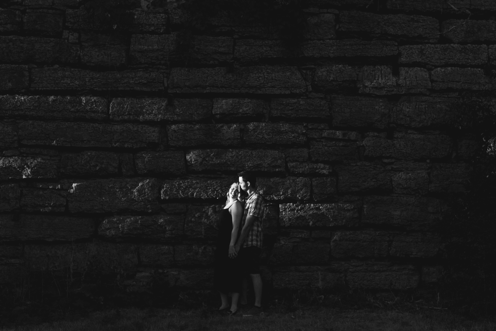 engaged couple standing in a pool of light against a brick wall