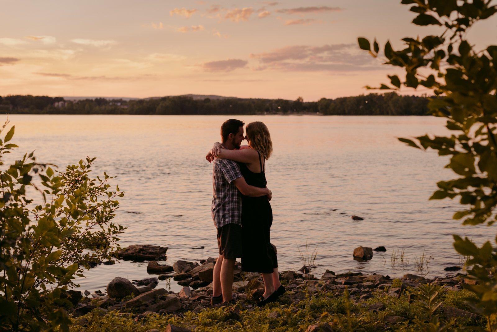 engaged couple hugging by the water at sunset