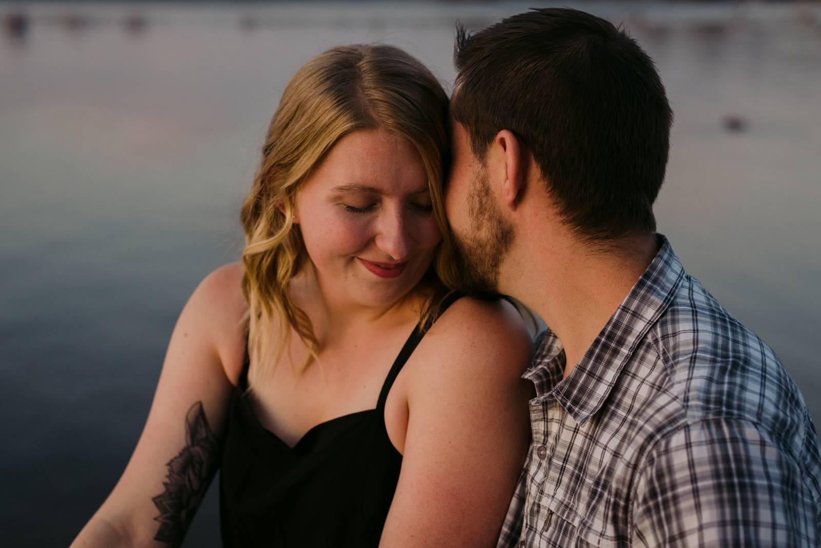 engaged couple cuddling by the water at sunset