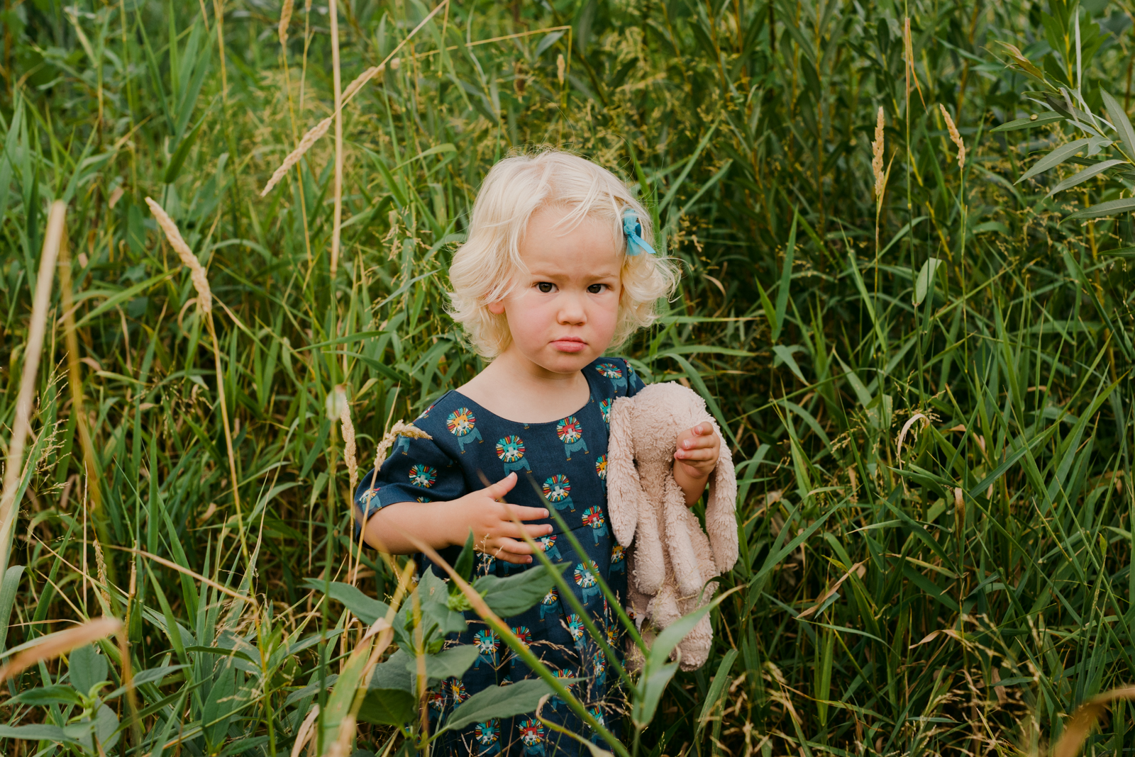 young blonde girl holding her rabbit in a field of long grass