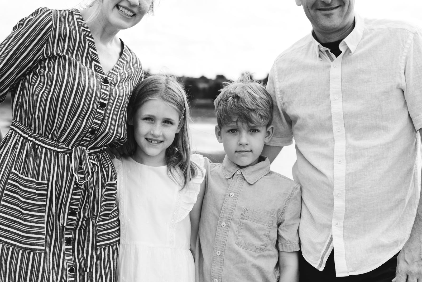 siblings smiling between their parents in black and white