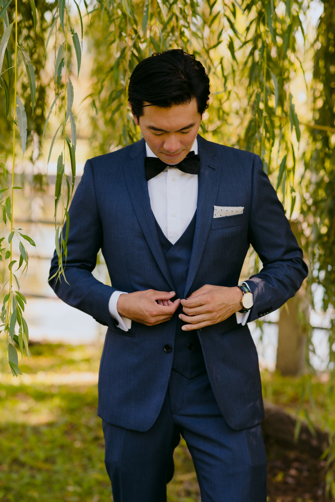 groom tying up his suit jacket underneath a willow tree by patterson's creek