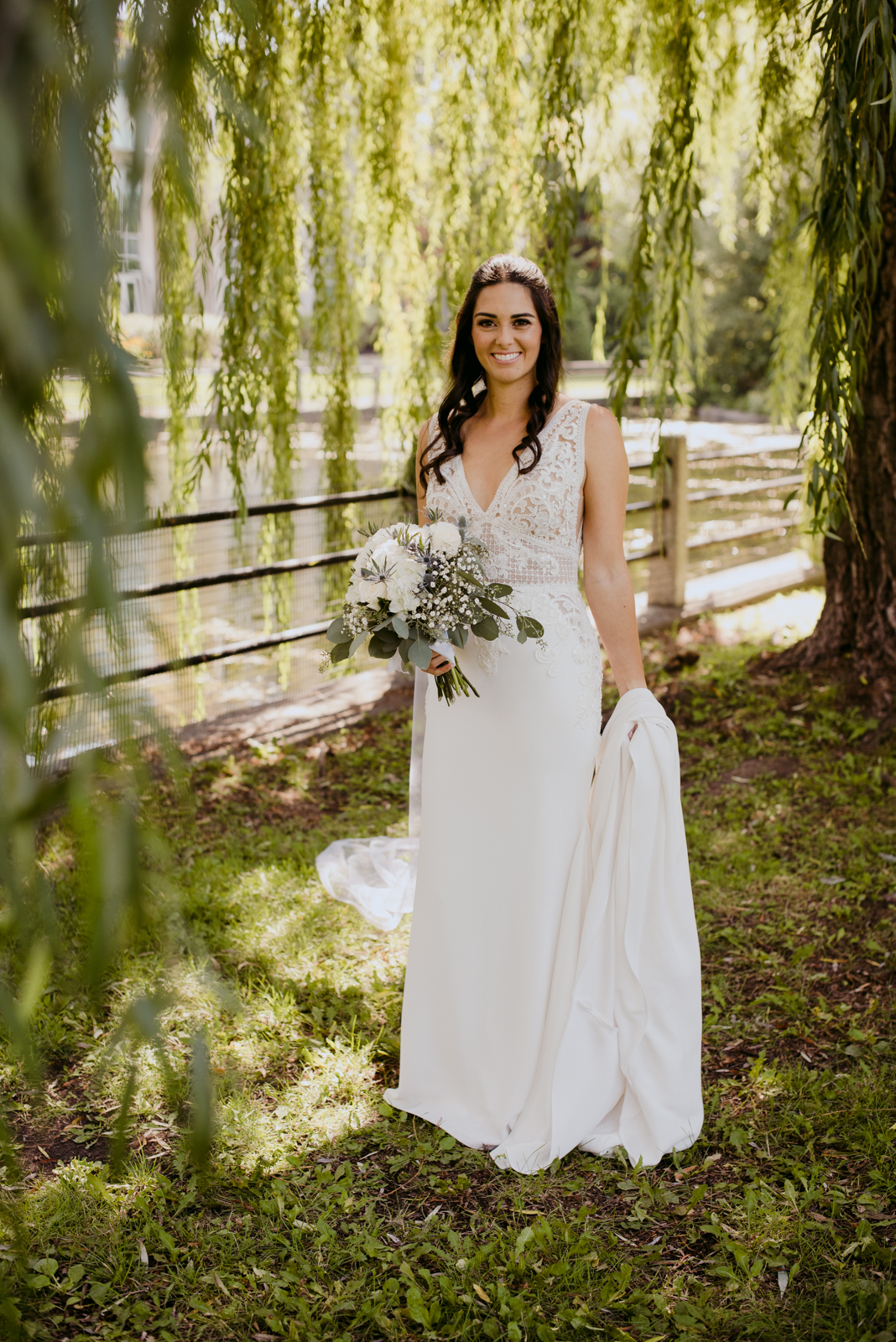 bride in the willow trees holding her train by patterson's creek