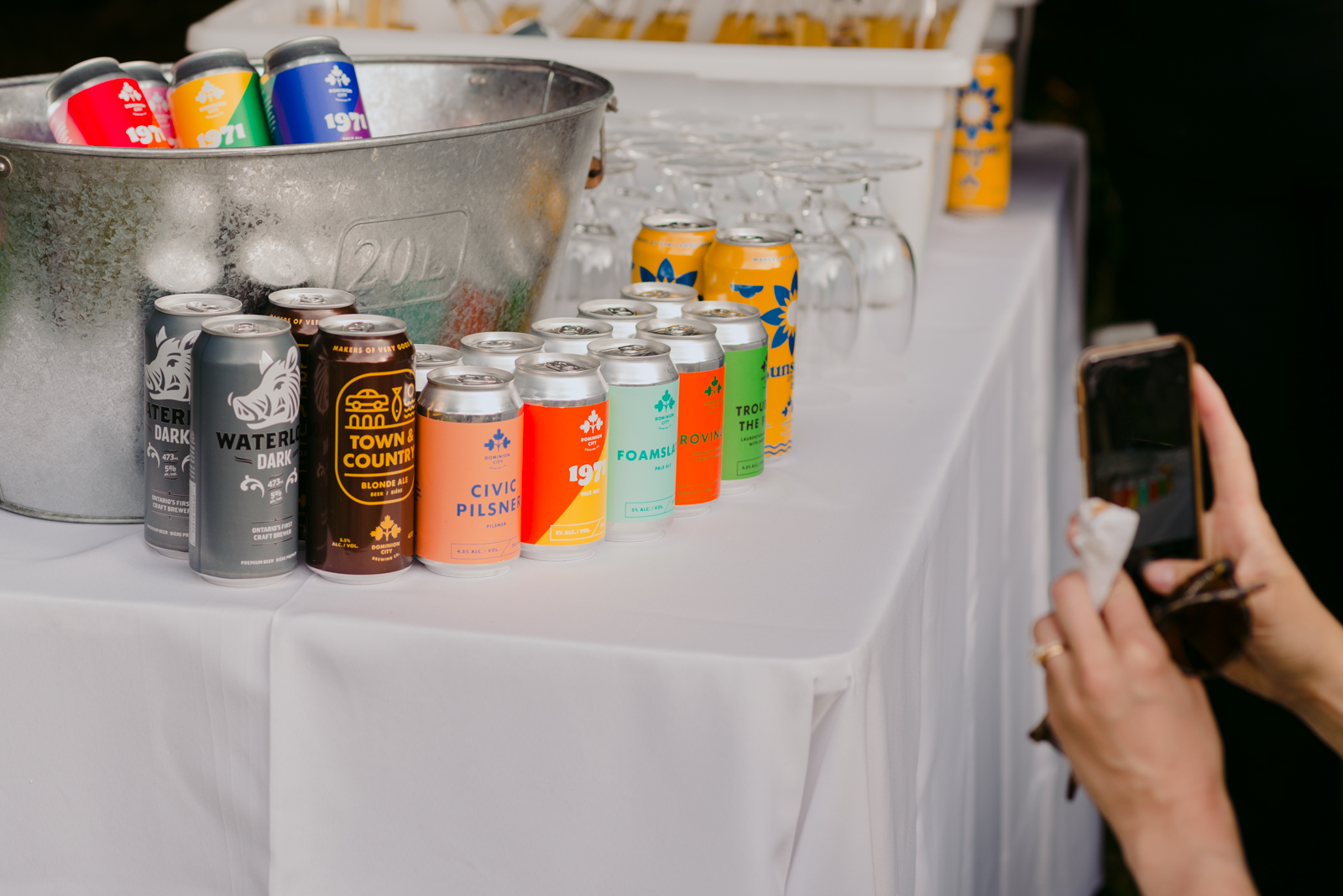wedding guest taking a photo of the lineup of Dominion City beer cans at cocktail hour