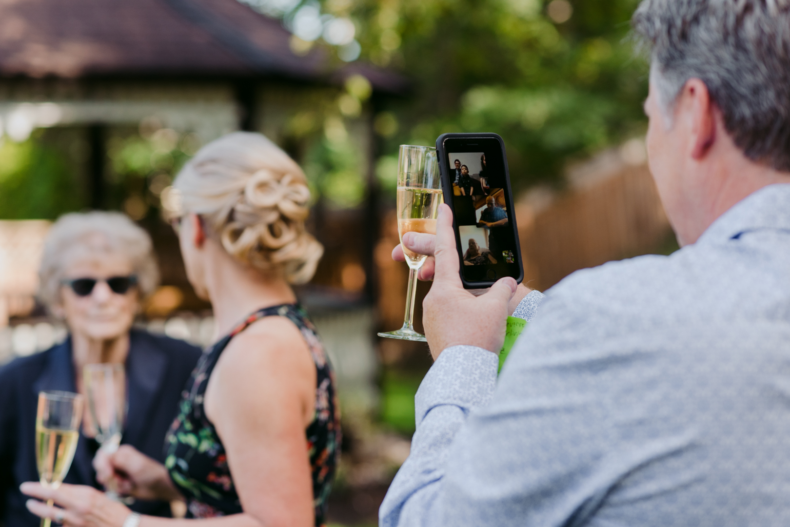 father of the bride holding phone with family live streaming wedding ceremony during champagne toast