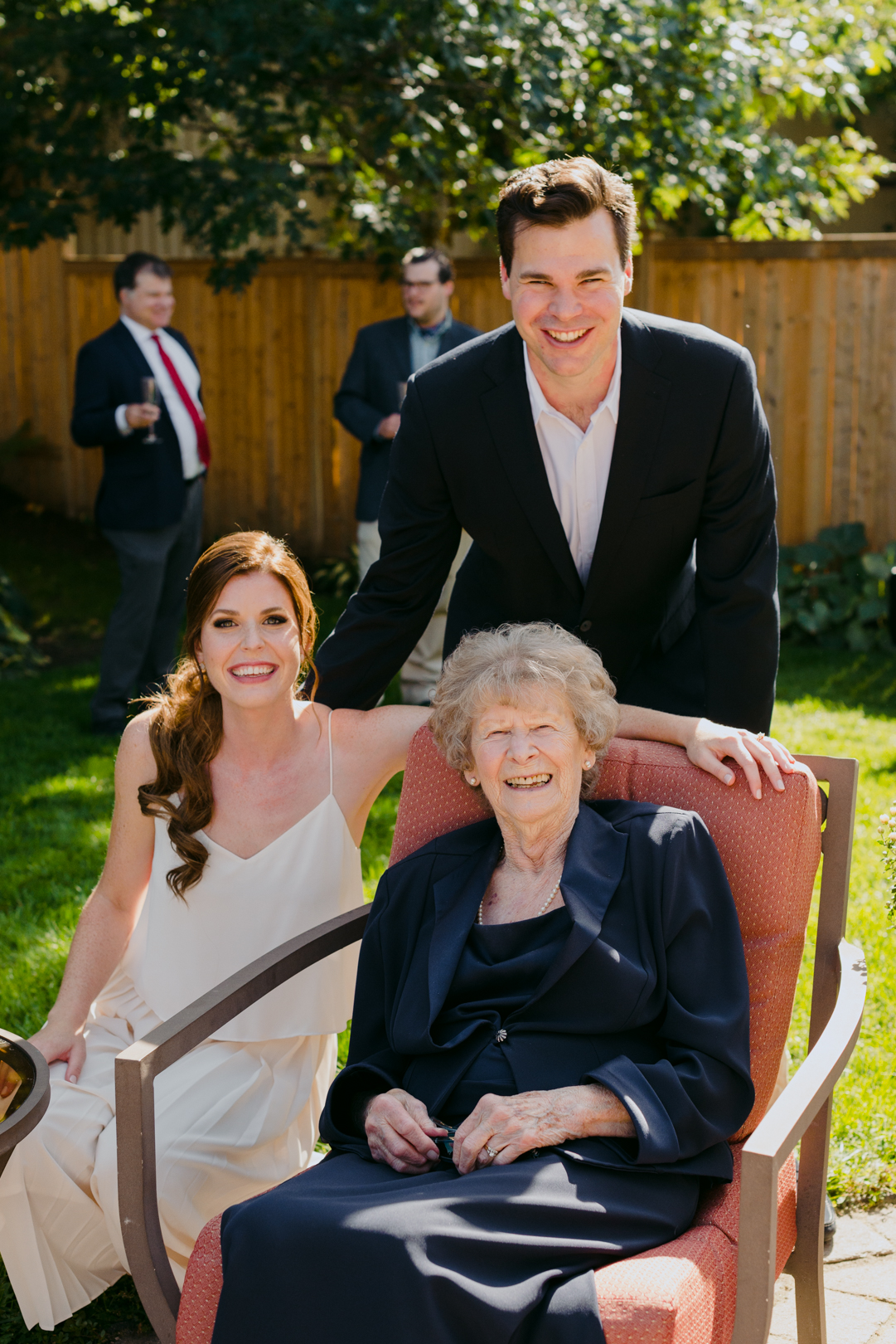 bride and groom posing with grandmother sitting in a chair